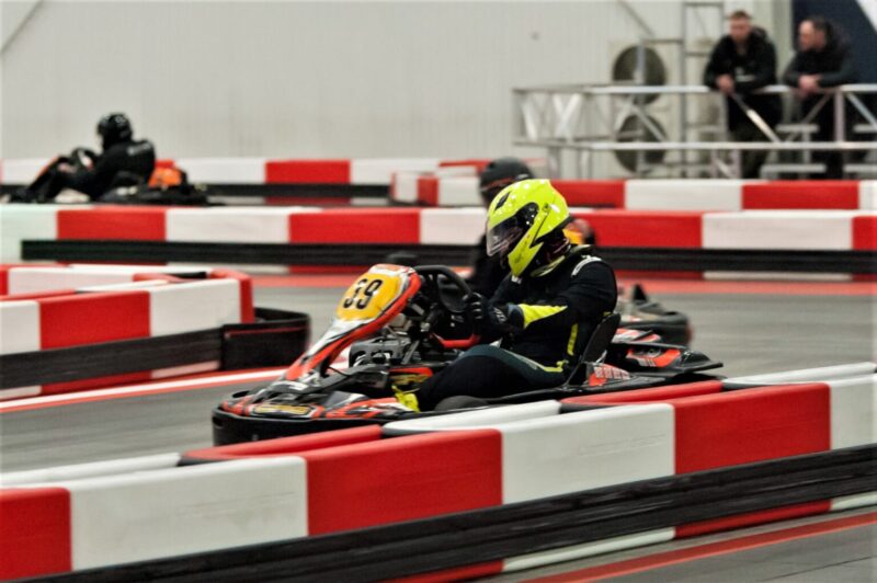 Dynamiczne ujęcie dwóch gokartów elektrycznego i spalinowego, ścigających się na zakręcie halowego toru kartingowego A1 Karting.